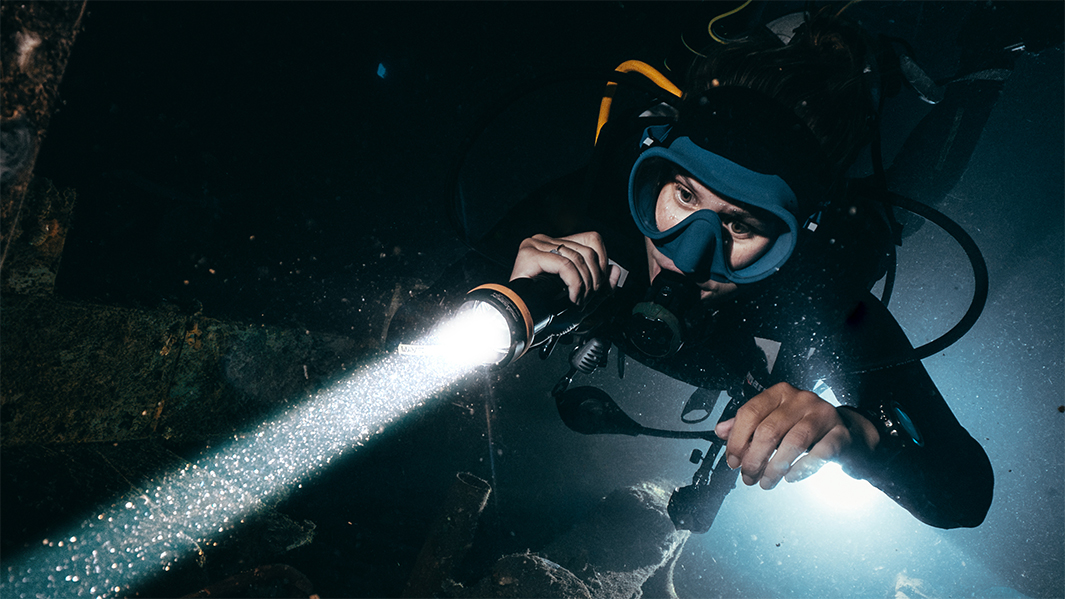 夜間ダイビングで強力な水中ライトを使用するプロスキューバダイバー 海中探索